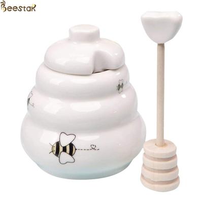 中国 卸し売り白い空の蜂蜜の瓶の蜂蜜の貯蔵のための木のディッパーが付いている陶磁器の蜂蜜の鍋 販売のため